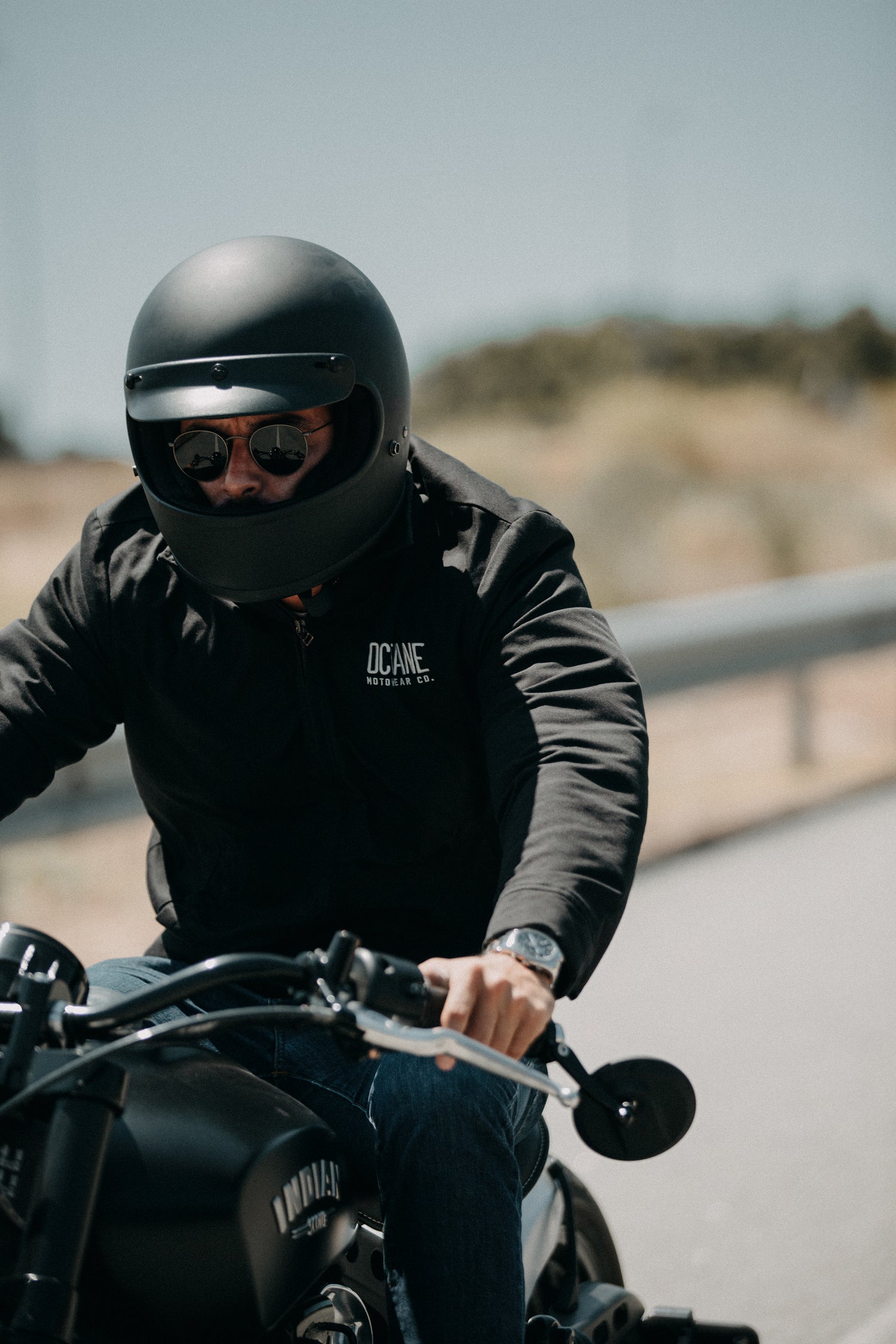 Rider riding Indian motorcycle with Octane Motowear jacket and black helmet.